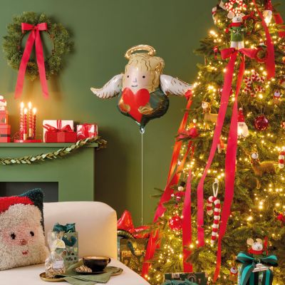 Christmas scenery with a christmas tree with lots of lights and bows, a balloon in shape of an angel and a sofa with a hooked santa claus pillow