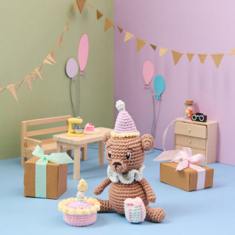 Ein brauner gehäkelter Bär mit Partyhut in einer gebastelten Partyszenerie.